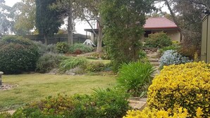 Un jardin bien entretenu, avec différentes espèces de plantes et un chemin qui mène à un bâtiment doté d’un toit rouge.