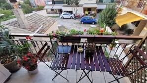 A balcony with a wooden table and chairs, potted plants, and a view of the street below. - Mon Repo Nest (Corfu)