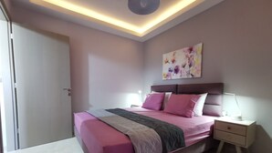 A bedroom with a bed, nightstands, a ceiling light, and a wall painting. - Mon Repo Nest (Corfu)