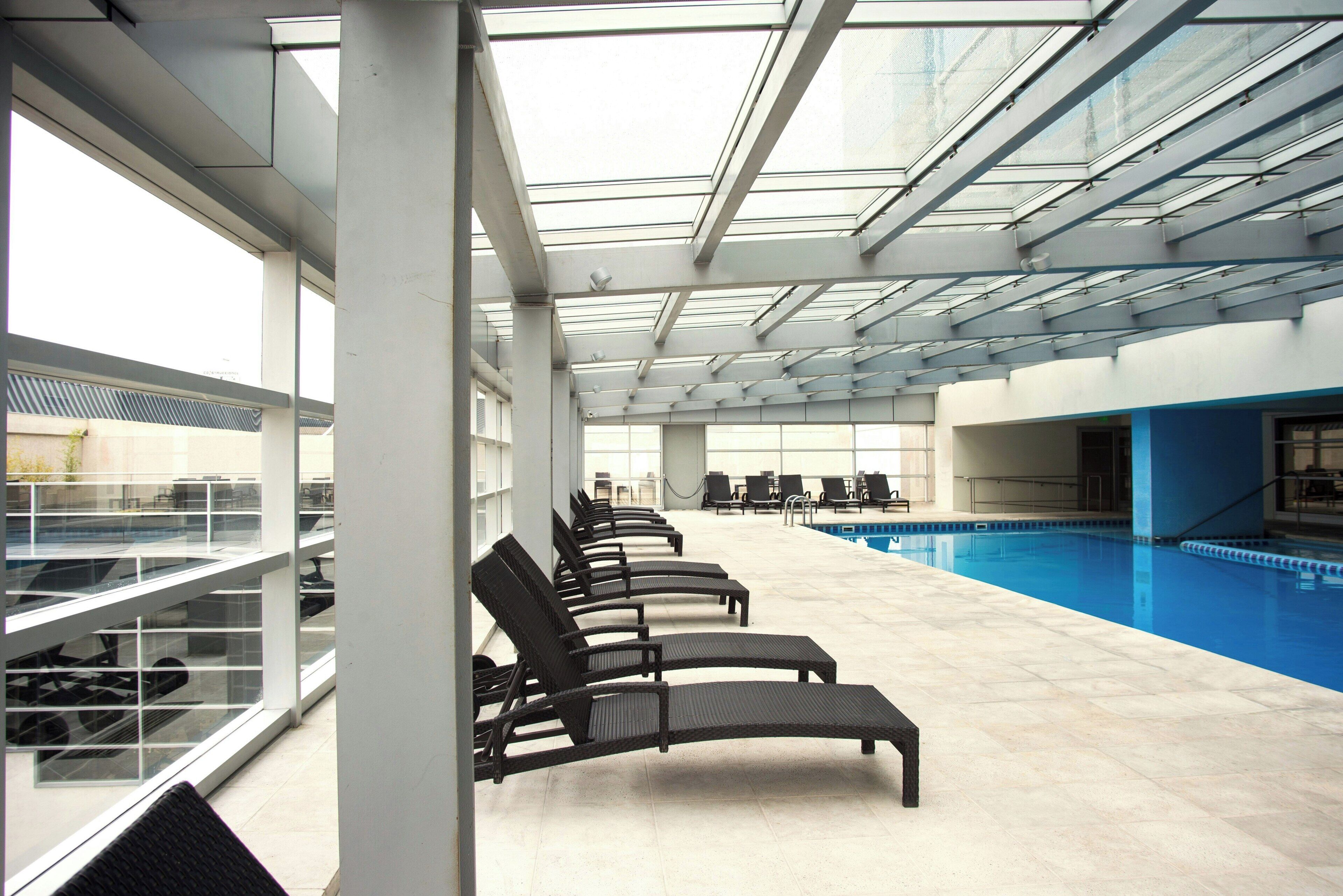 A pool area with lounge chairs and a glass ceiling.