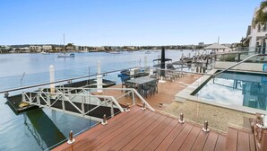A marina with boats docked, a pool area with lounge chairs, and a cityscape in the background.
