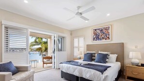 A bedroom with a bed, a chair, a bedside table, a ceiling fan, and a view of the outdoors.