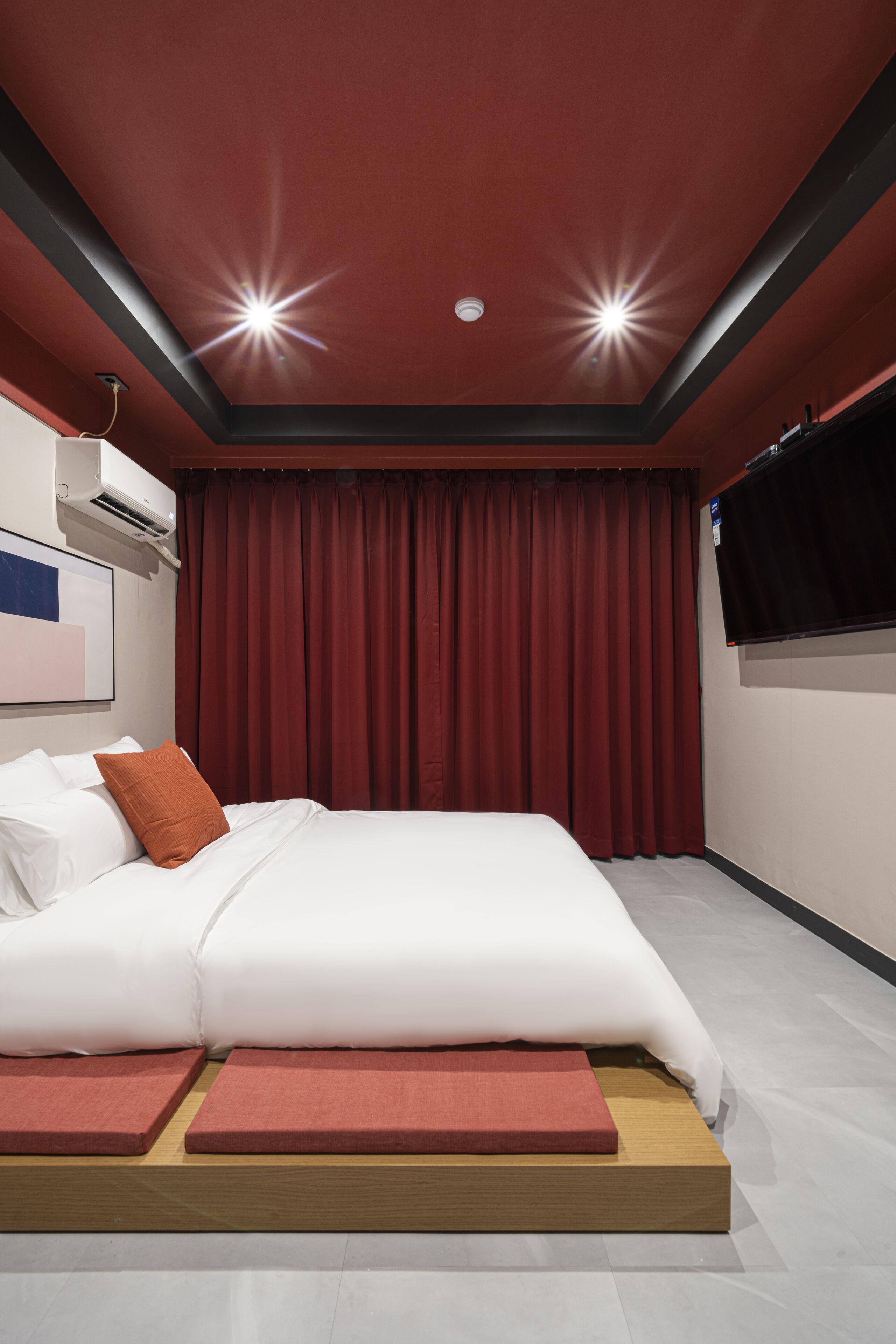 Una habitación de hotel moderna con una cama grande, cortinas rojas y un televisor montado.