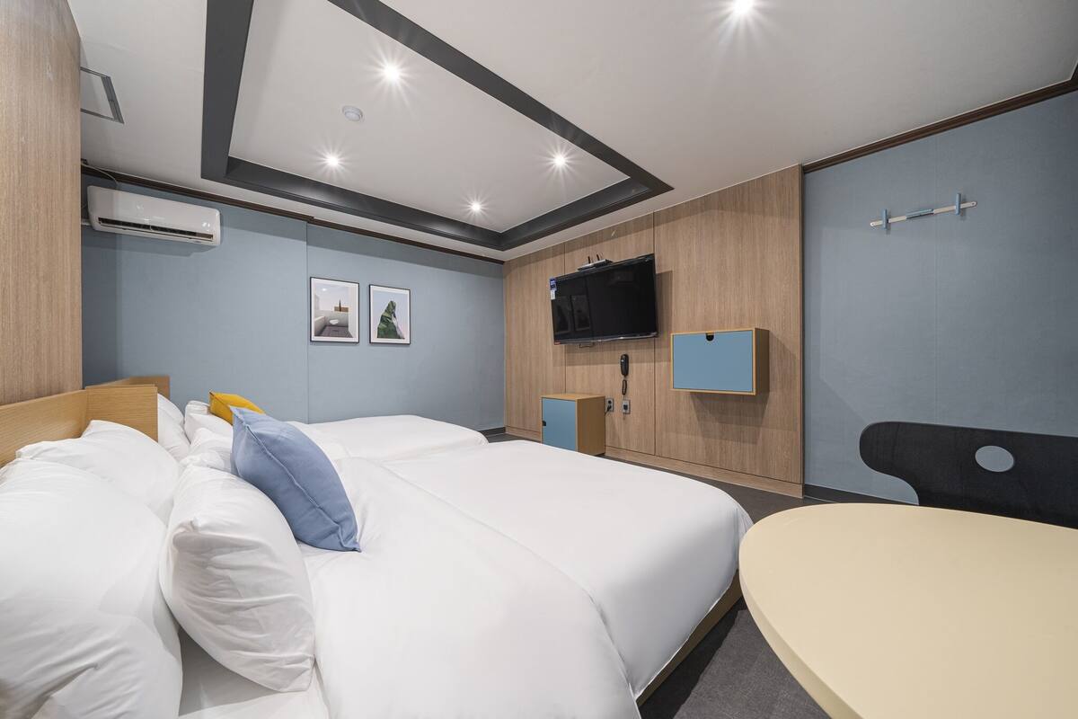 A modern hotel room with a large bed, a desk, a flat-screen TV, and an air conditioning unit.