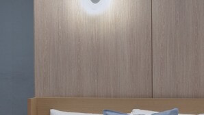 A neatly made bed with white and blue pillows, a wooden headboard, and a wall-mounted light fixture. - The Shourin in Daejeon (Daejeon)
