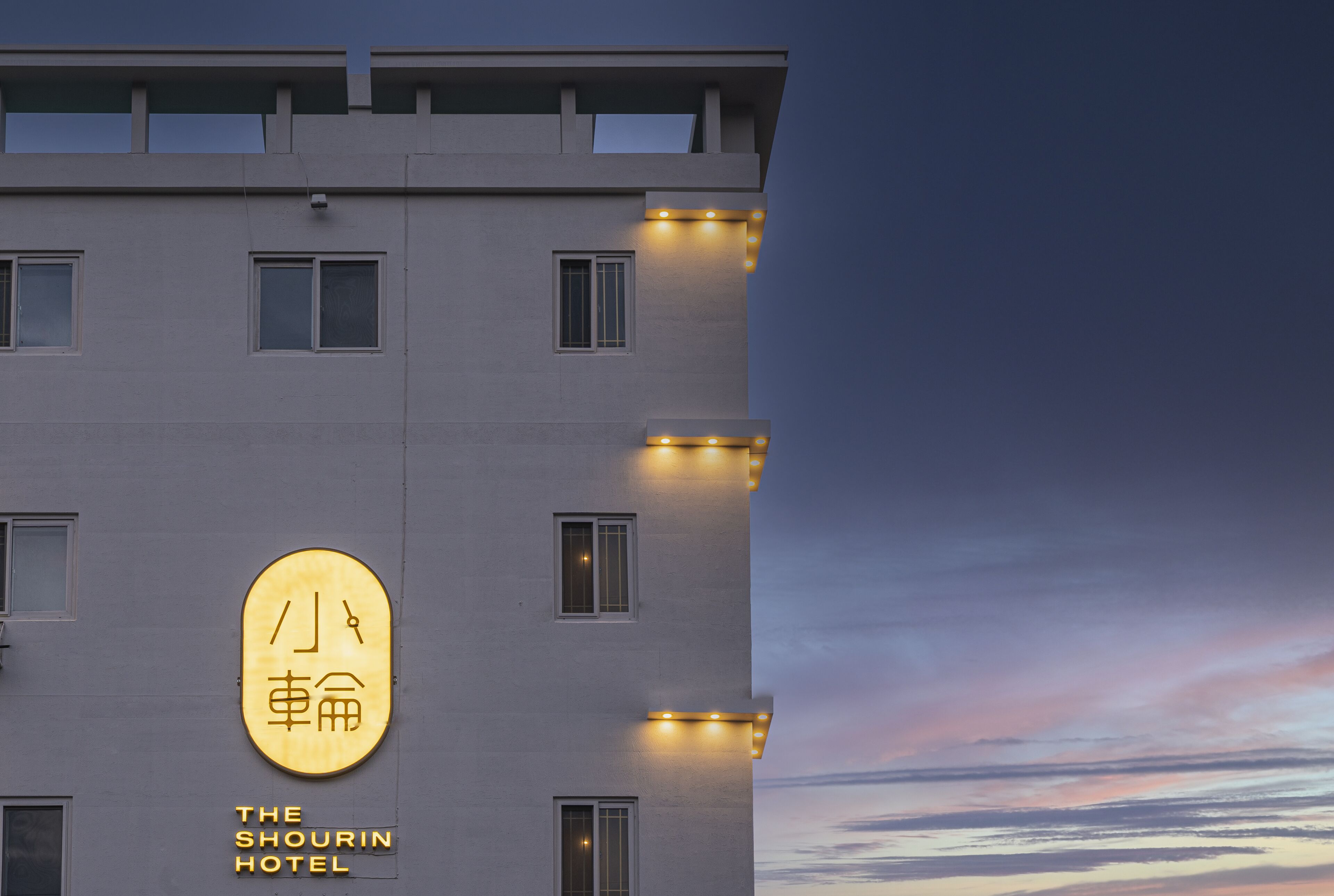 Ein Hotelgebäude mit einem Schild, auf dem 'The Shorin Hotel' steht, und einer großen, beleuchteten Beschilderung mit chinesischen Schriftzeichen.
