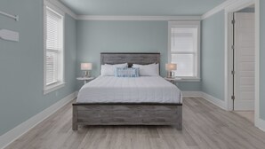 Une chambre à coucher avec un lit, deux tables de chevet, un ventilateur de plafond et une porte.