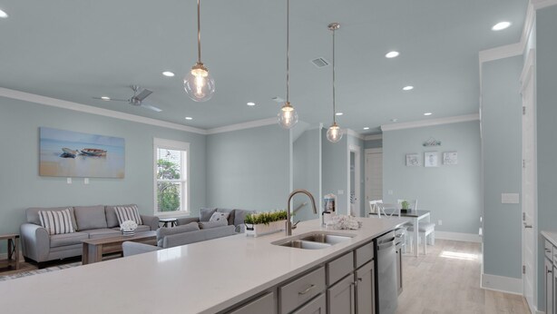 Une cuisine moderne dotée d’un grand îlot central, de luminaires suspendus et d’un coin repas avec une table et des chaises blanches.