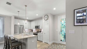 A modern kitchen with white cabinetry, stainless steel appliances, and pendant lighting.