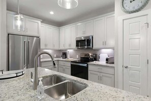 Una cocina moderna con gabinetes blancos, electrodomésticos de acero inoxidable, encimera de granito y microondas integrado.