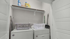 A laundry area with two washing machines, a shelf with cleaning supplies, and a broom.