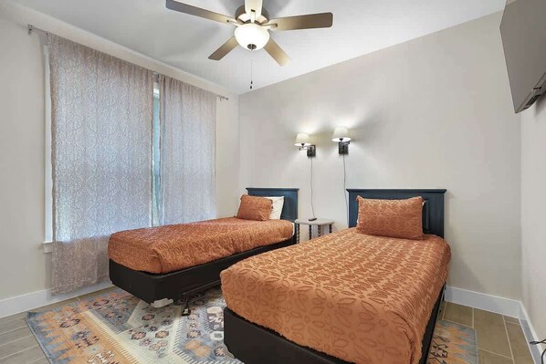 Ein Schlafzimmer mit zwei Betten, einem Deckenventilator, einem Fenster mit Vorhängen und zwei Wandleuchten.