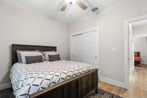 Un dormitorio con cama, ventilador de techo, una puerta blanca y un pasillo que conduce a otra habitación.