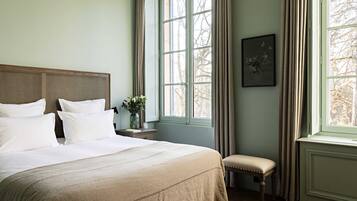 A bedroom with a large bed, a nightstand, a bench, and a window with curtains.
