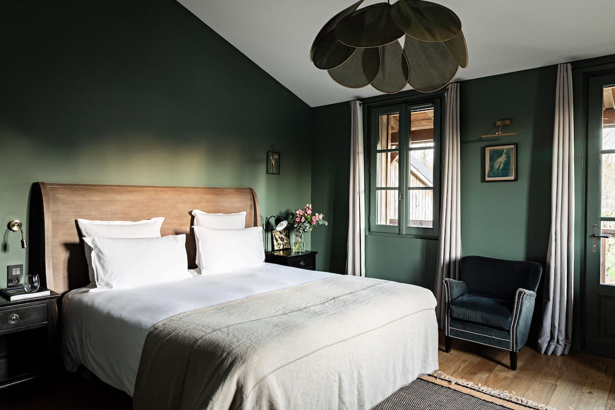 A neatly made bed with white linens, a dark wooden headboard, and a bedside table with a lamp and a small vase of flowers.