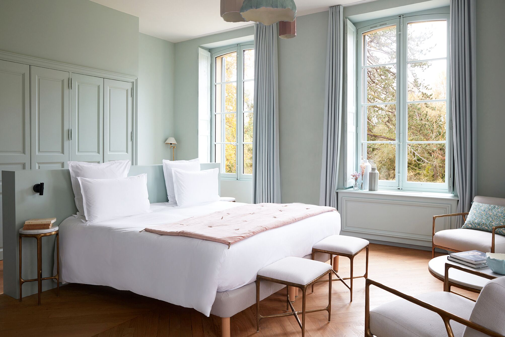 Un dormitorio con una cama grande, dos mesitas de noche, una silla y un ventanal con cortinas.