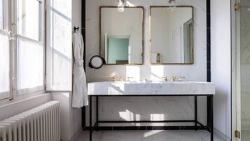 Un baño con lavamanos de mármol blanco, dos espejos con marcos dorados y un radiador blanco.