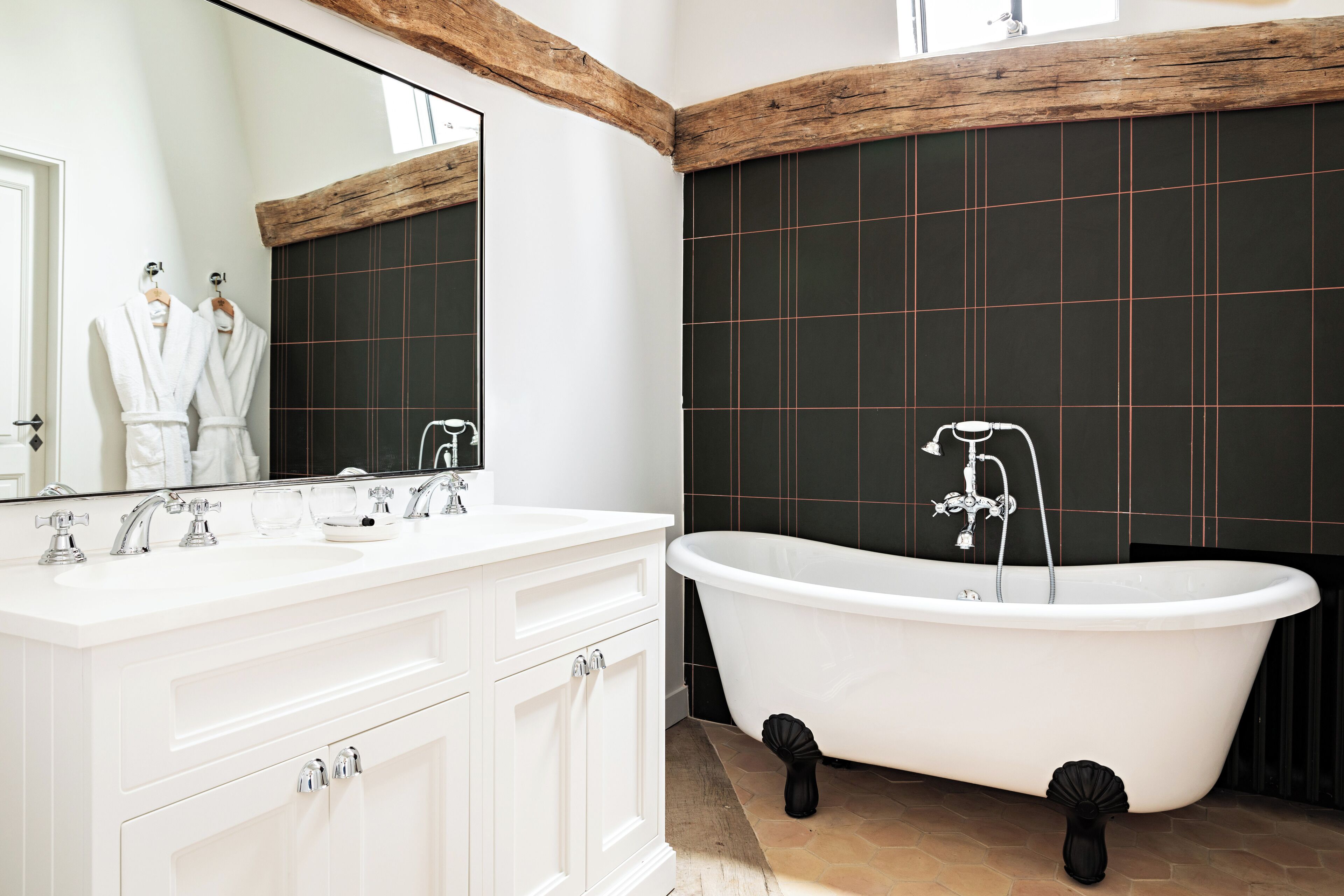 Une salle de bain avec une baignoire sur pieds, un grand miroir et des meubles de rangement blancs.