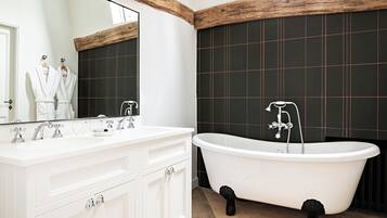 Une salle de bain avec une baignoire sur pieds, un grand miroir et des meubles de rangement blancs.