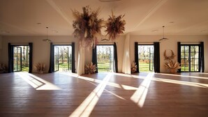 Amplia habitación con ventanas grandes, suelo de madera y arreglos florales colgantes.