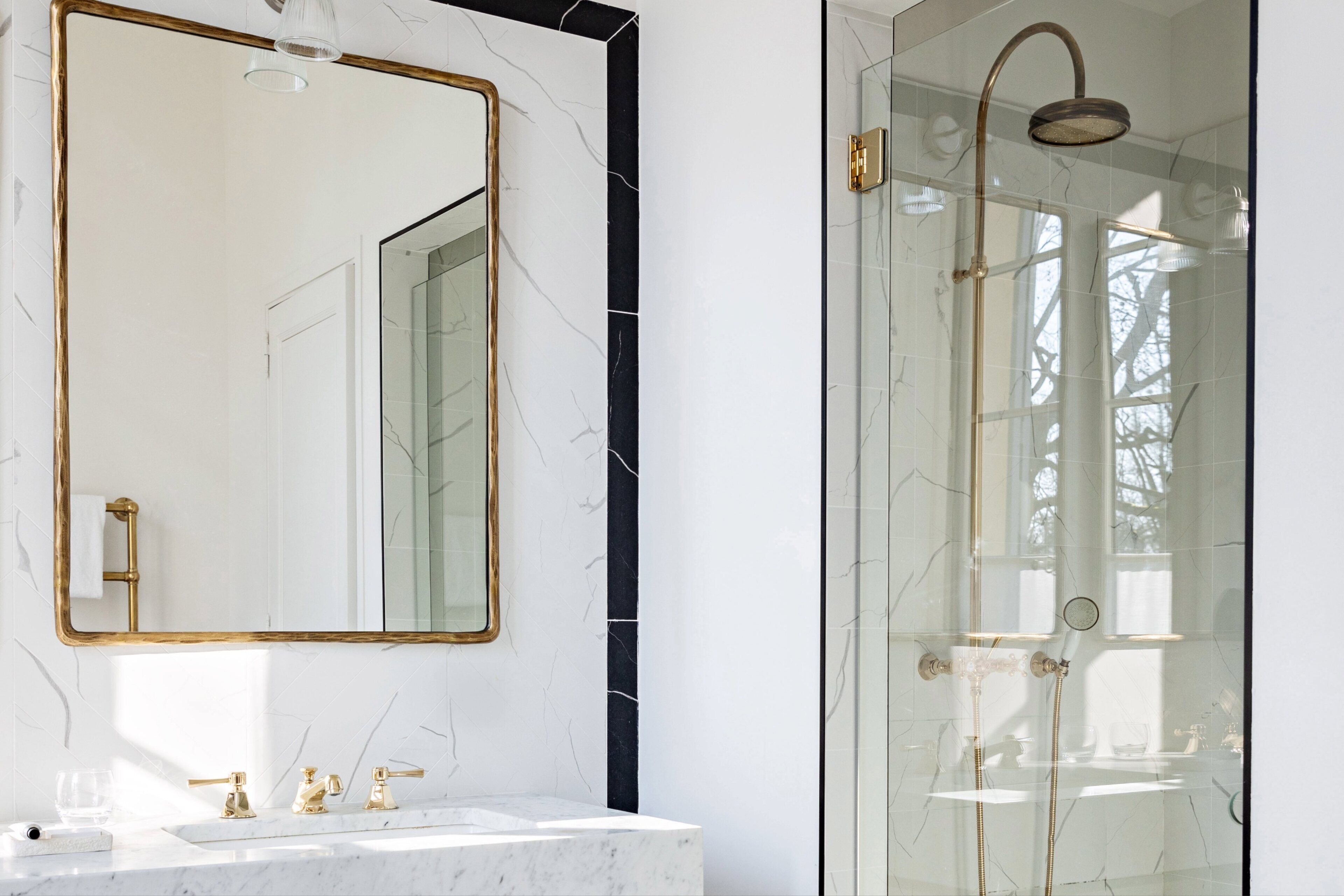 A bathroom with a marble vanity, a gold-framed mirror, and a glass-enclosed shower.