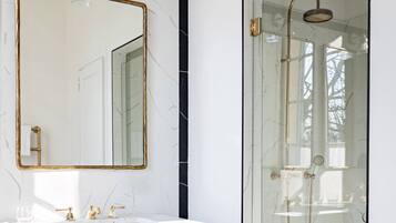 A bathroom with a marble vanity, a gold-framed mirror, and a glass-enclosed shower.