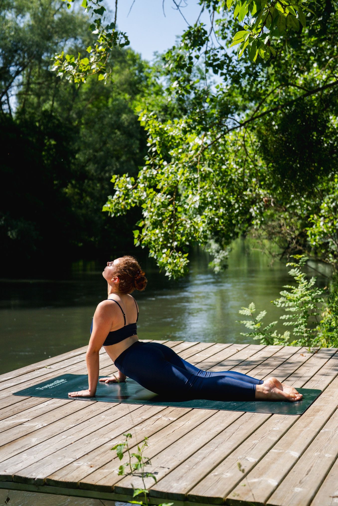A person sitting on a wooden dock by a river, surrounded by greenery.