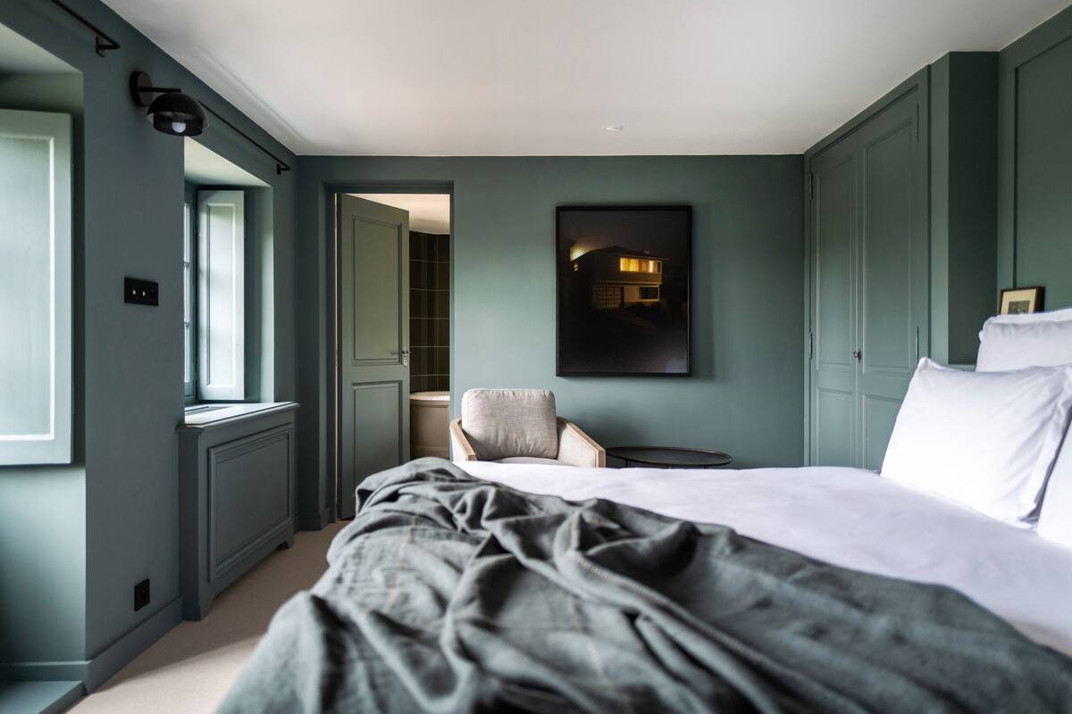 A bedroom with a large bed, a chair, a small table, and a framed picture on the wall.