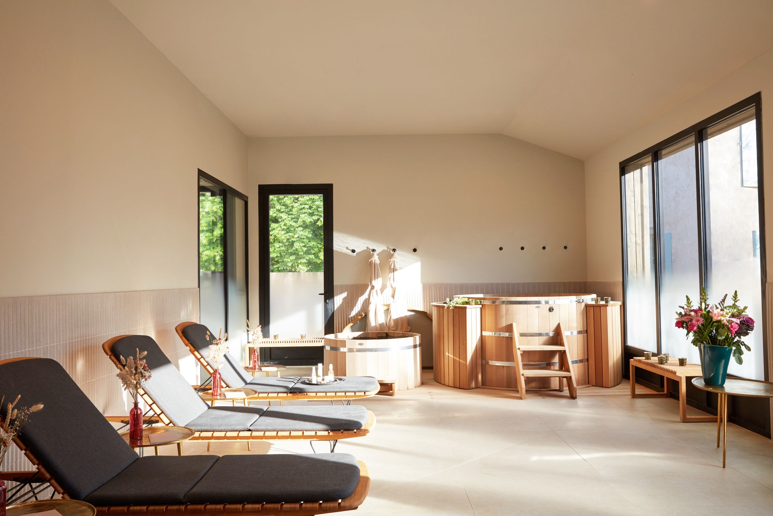 A modern spa room with multiple massage tables, a sauna area, and large windows providing natural light.
