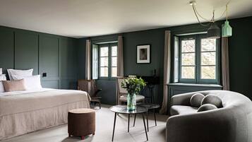 A room with a bed, two chairs, a small table with a vase, and a sofa.