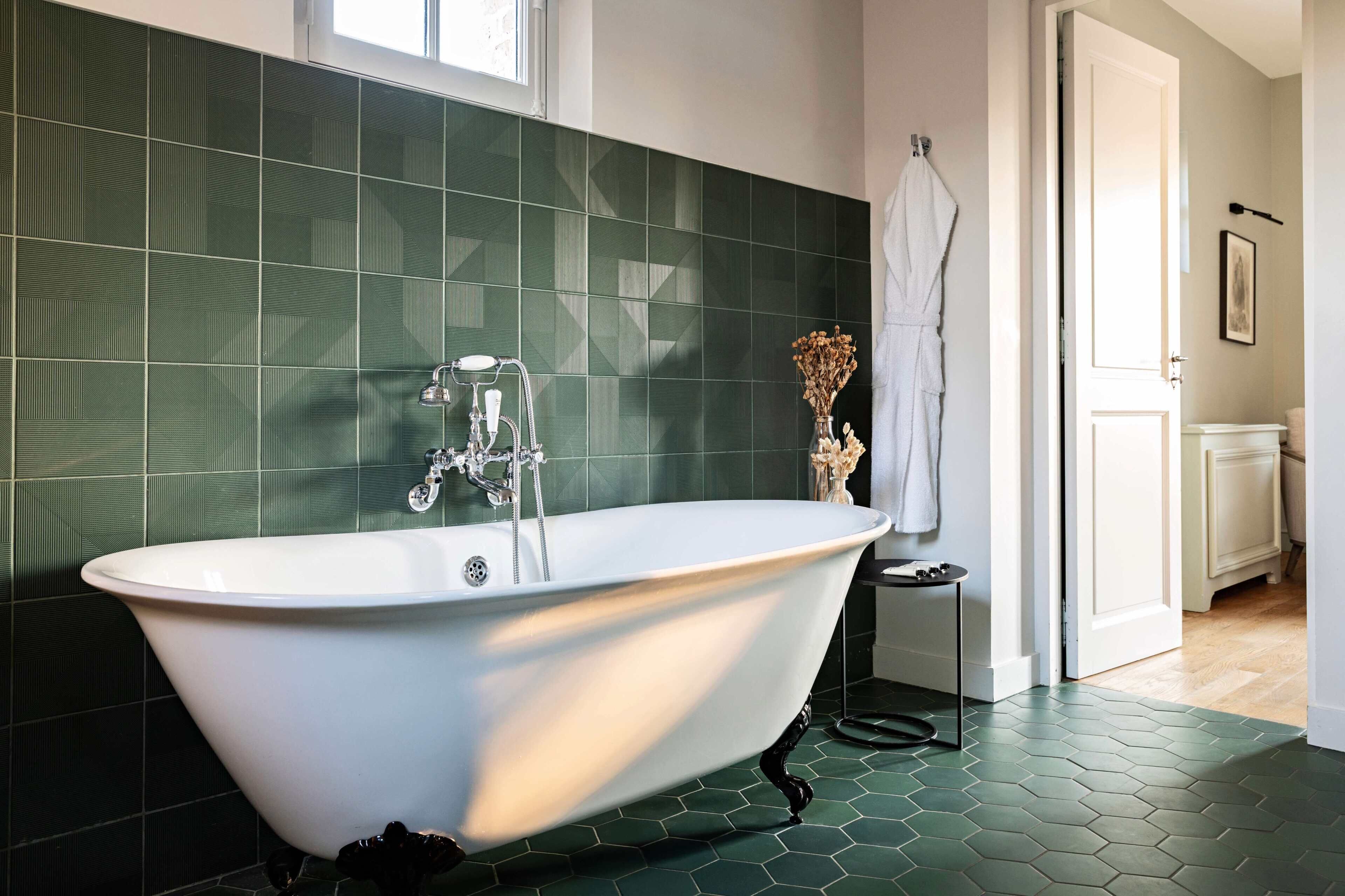 A modern bathroom with a freestanding bathtub, green hexagonal tiles, and a white door leading to another room.