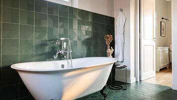 A modern bathroom with a freestanding bathtub, green hexagonal tiles, and a white door leading to another room.