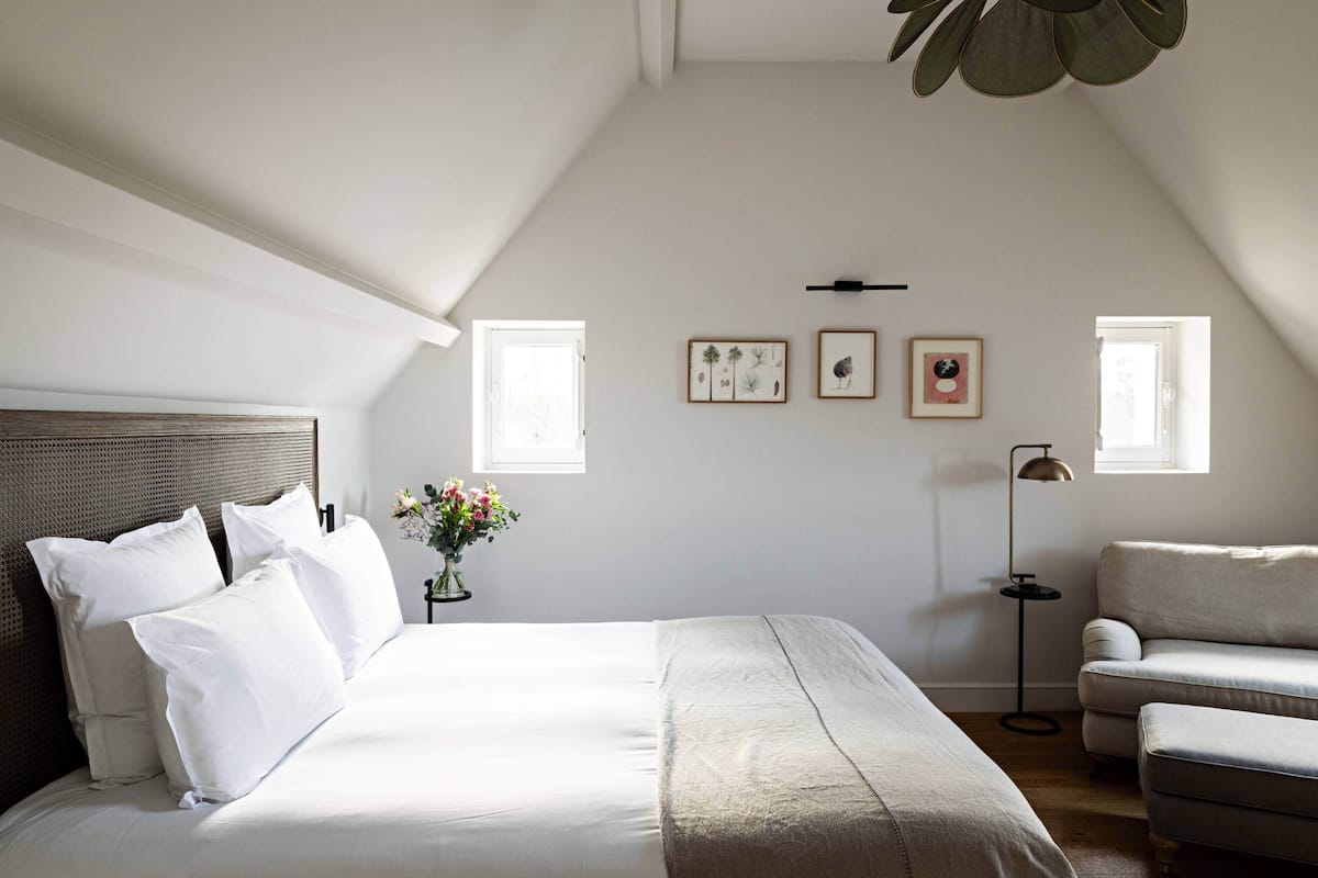 A bedroom with a large bed, a sofa, a floor lamp, and framed botanical prints on the wall.