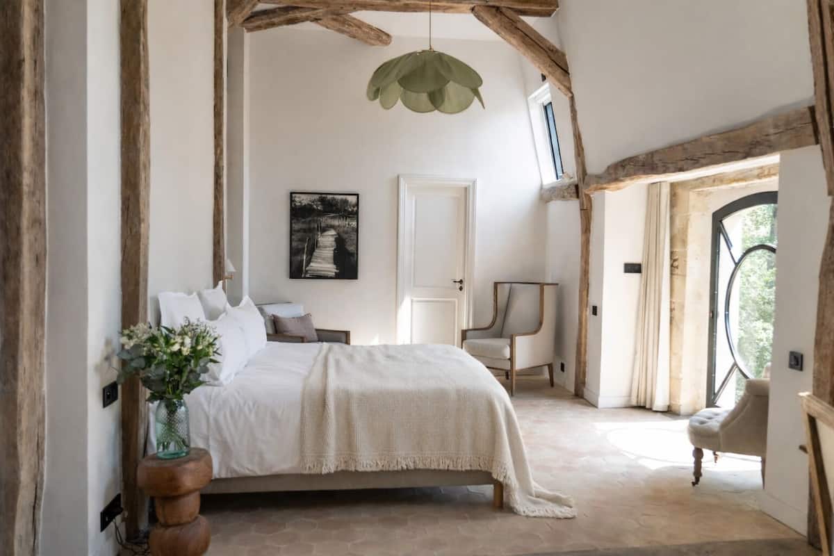 A bedroom with a bed, a chair, a desk, a window, and a door.