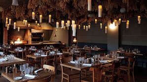 Un restaurante con mesas y sillas de madera, velas colgantes y una pared de ladrillo con chimenea.