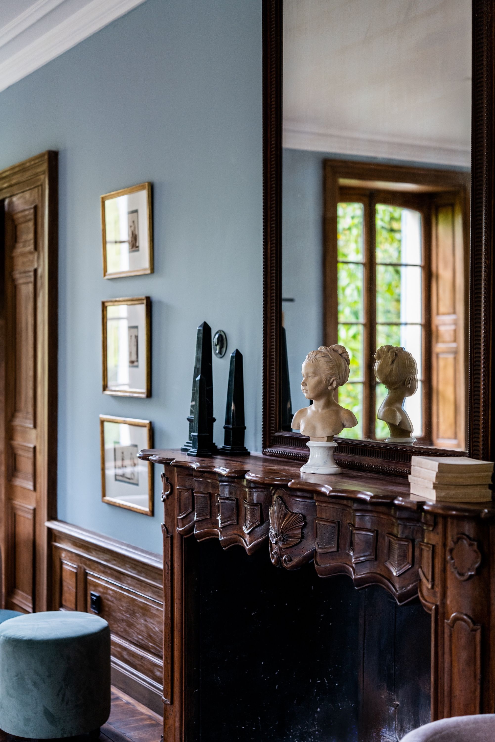 Une pièce dotée d’un grand miroir qui reflète une fenêtre, d’un bureau en bois orné d’un buste sculpté et de tableaux encadrés accrochés au mur.