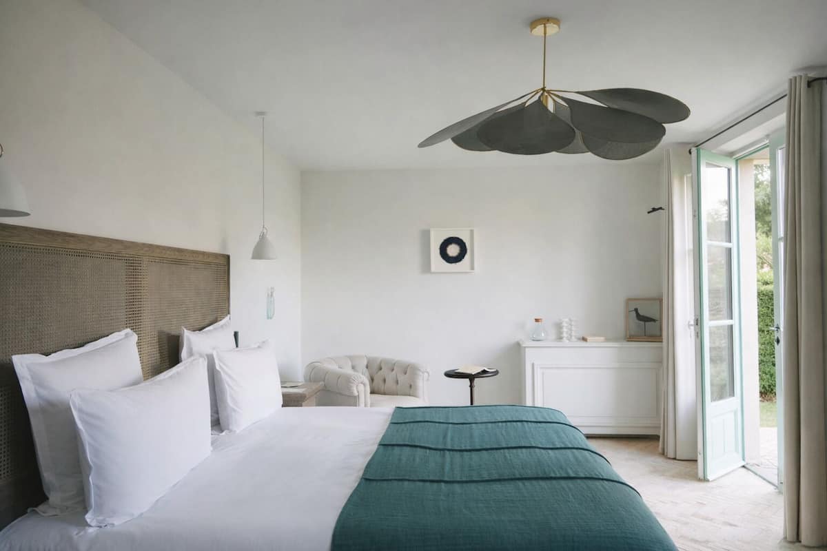 A bedroom with a large bed, a bedside table, a chair, and a view of the outdoors through a door.