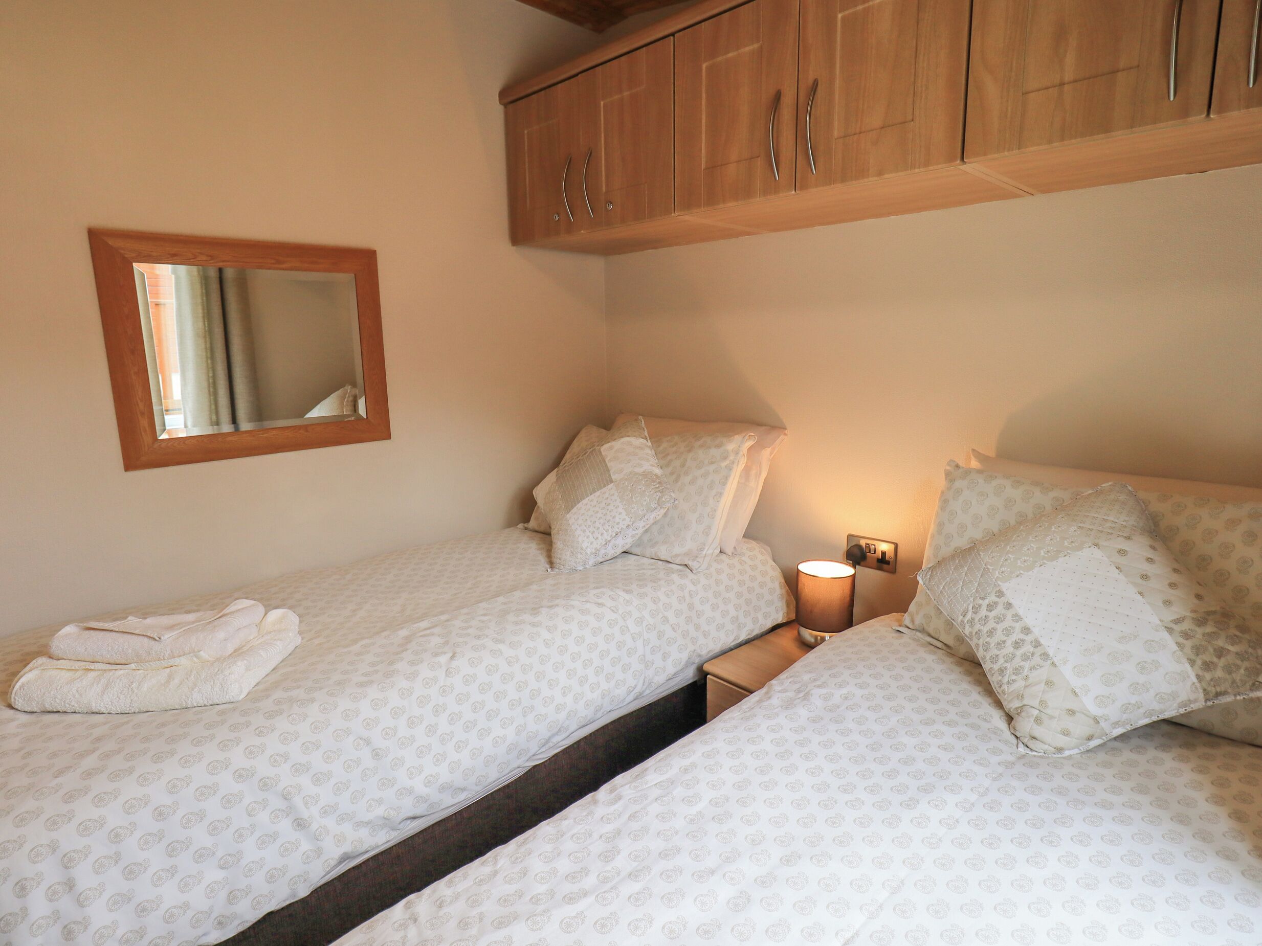 A bedroom with two beds, a mirror, and a nightstand with a lamp.