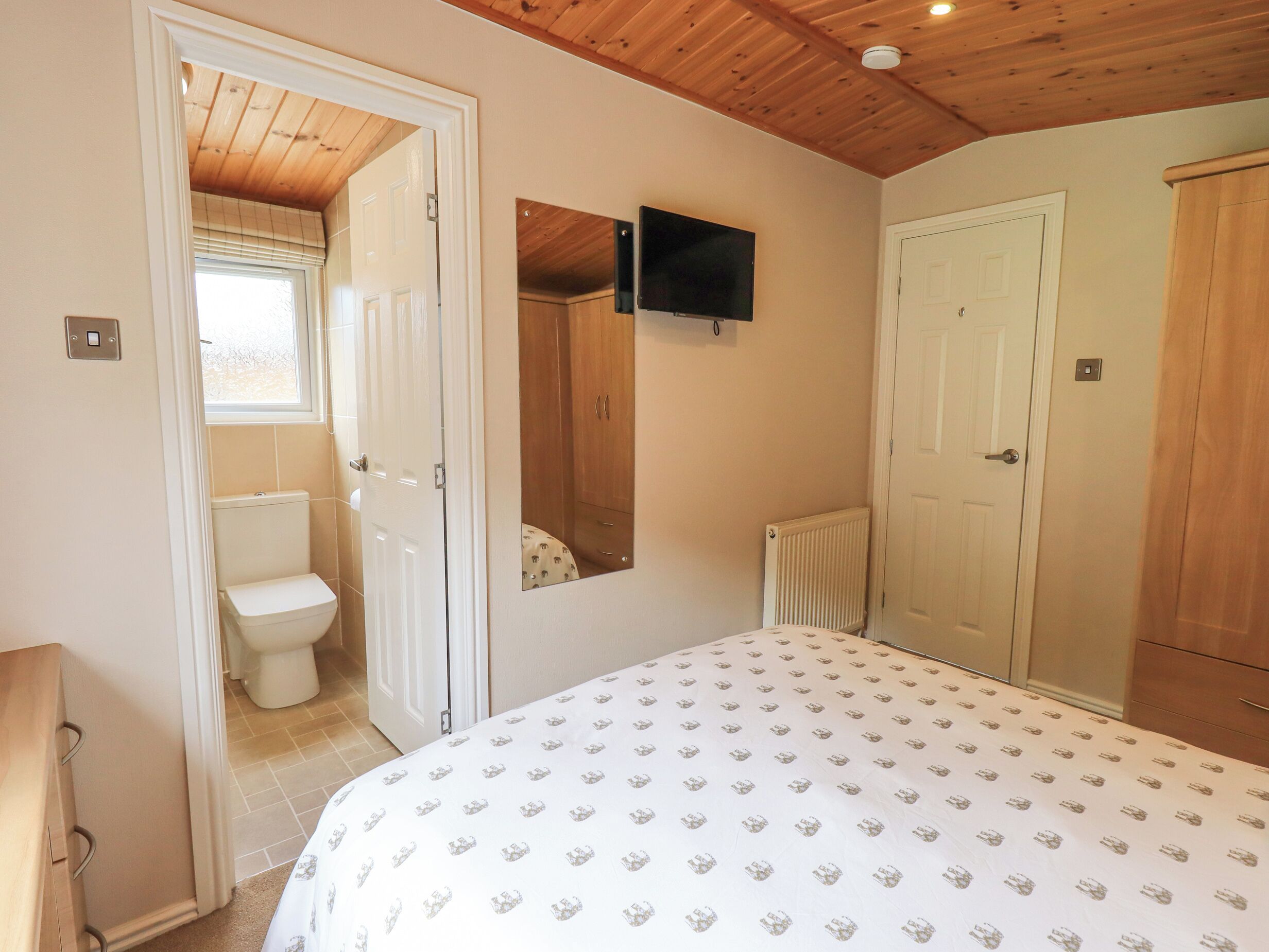 Een slaapkamer met een bed, toilet, spiegel en televisie.