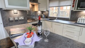 A modern kitchen with a gas stove, a built-in oven, a sink, and a window with a view of a fence. - Lavender Lodge (Windermere)