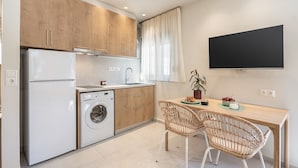 Une cuisine compacte avec des meubles en bois, un lave-linge, un évier et un coin repas avec des chaises en osier.