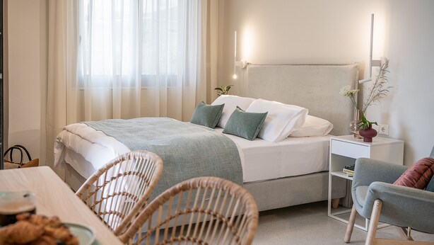 Une chambre bien rangée, avec un lit, une table de chevet, une chaise et un coin repas comprenant une table et des chaises.