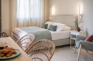 Un dormitorio ordenado con cama, mesita de noche, silla y un área de comedor con mesa y sillas.