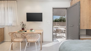 Une chambre moderne avec un lit, une télévision et un coin repas comprenant des chaises et une table en osier.