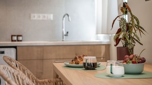 Une table de petit-déjeuner avec des viennoiseries, du café et des fruits, dans une cuisine moderne.