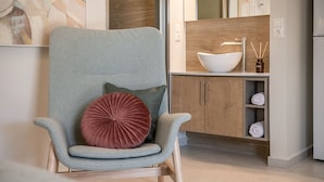 Une cuisine moderne avec une chaise à revêtement gris, un évier-bol blanc, des meubles en bois et une étagère à serviettes.