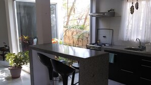 Uma cozinha moderna com uma ilha central, banquetas, fogão a gás e vista para o exterior através de uma grande janela.