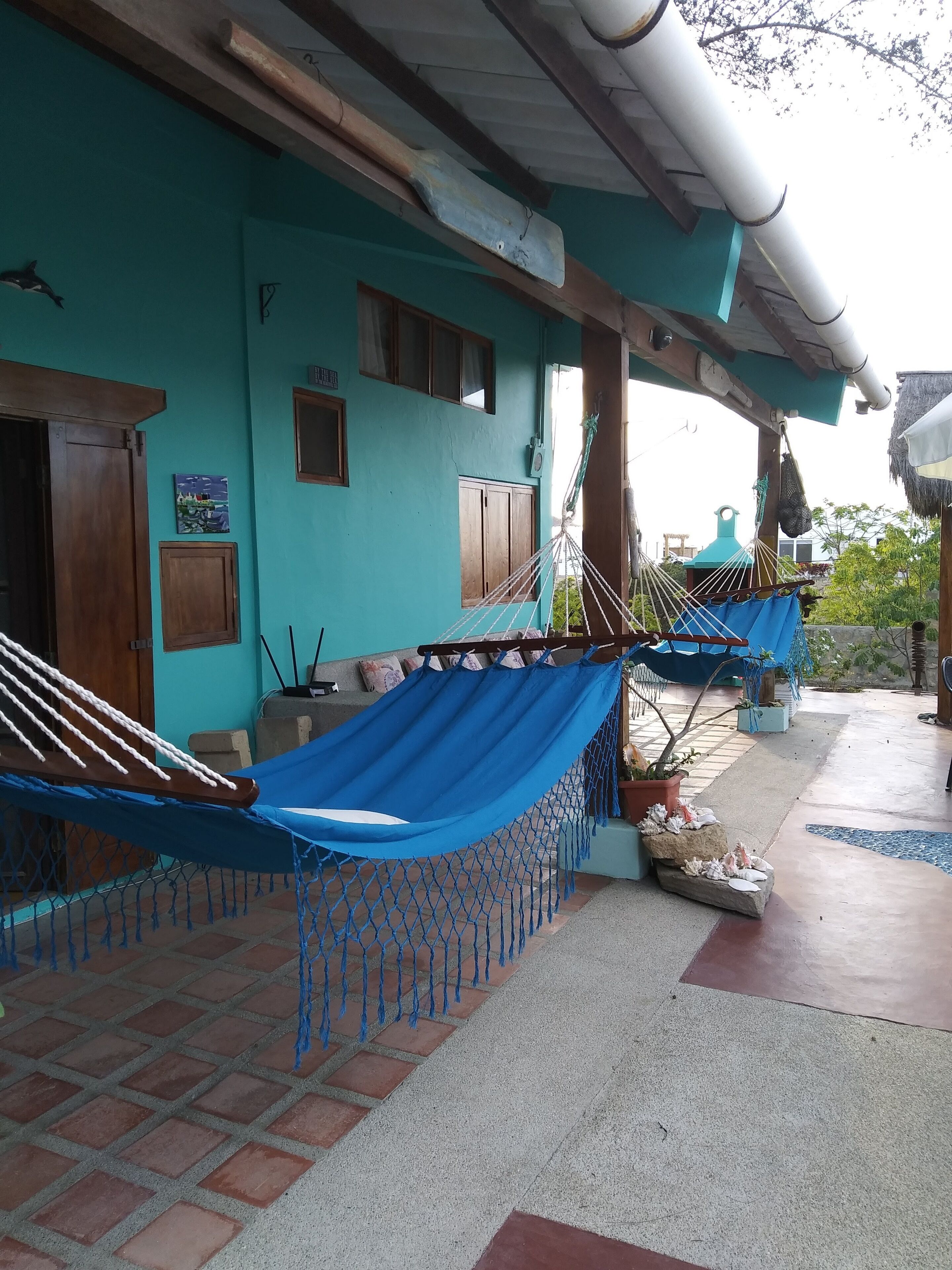A hammock under a wooden structure with a tiled floor and a blue wall.