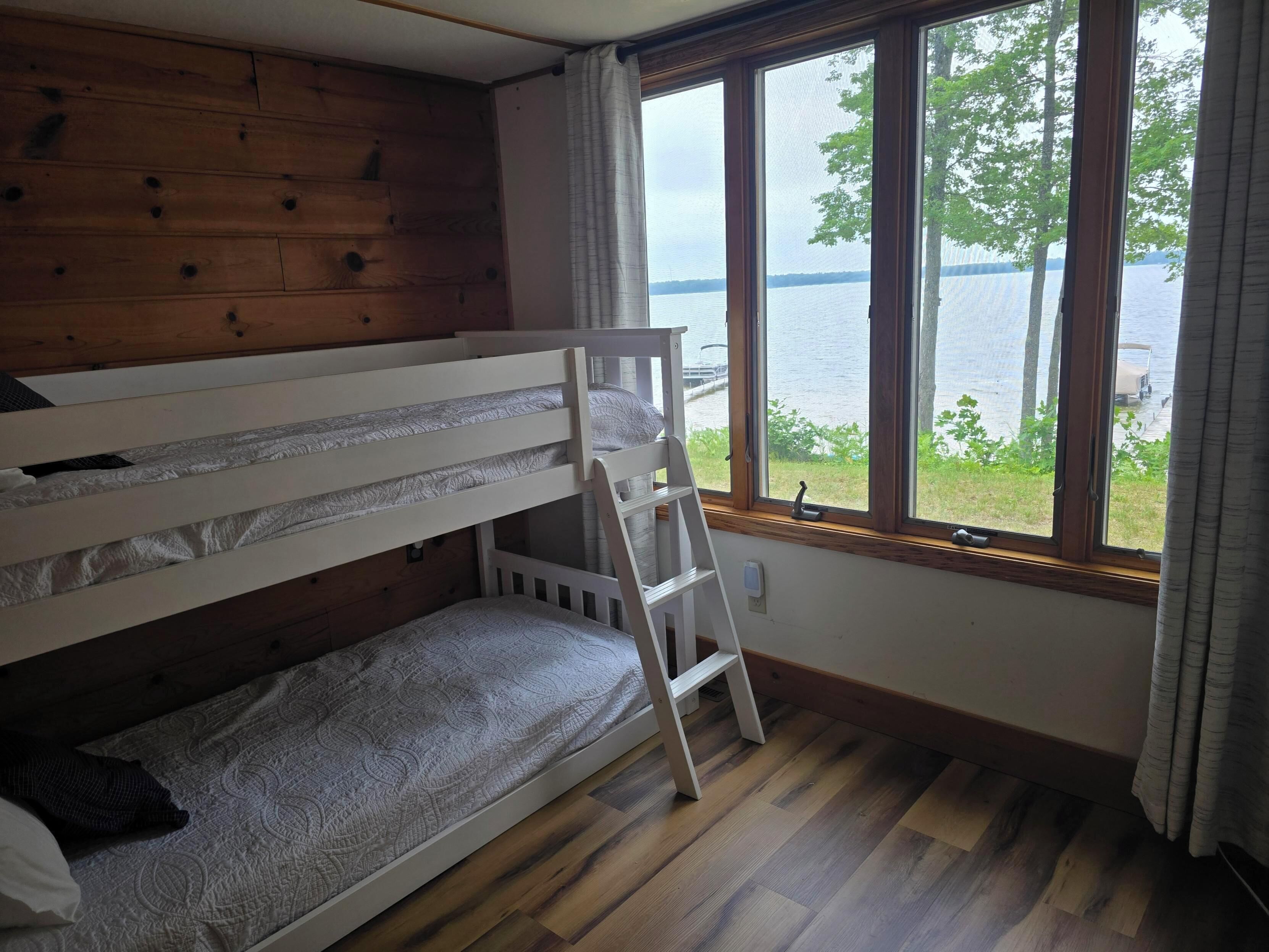Camera con letto a castello, parete in legno, finestra vista lago e scaletta.