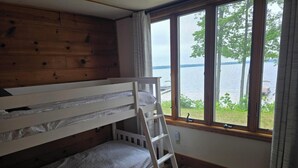 A bunk bed room with a wooden wall, a window with a view of a lake, and a ladder.